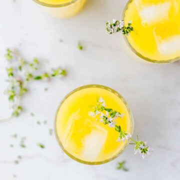 homemade mango lemonade served in glasses with ice cubes and fresh thyme