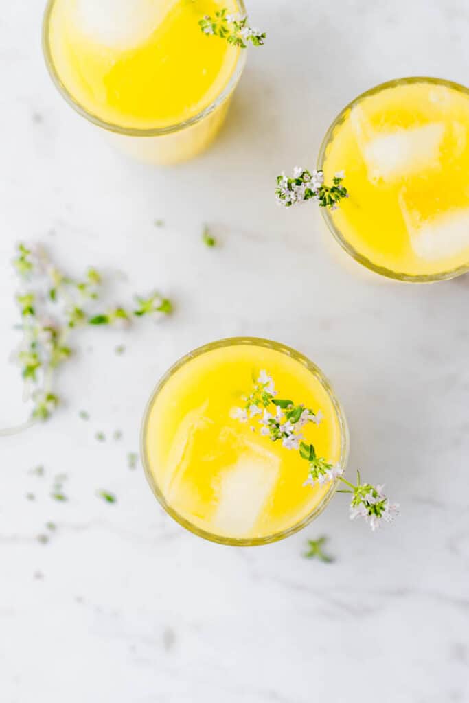 homemade mango lemonade served in glasses with ice cubes and fresh thyme