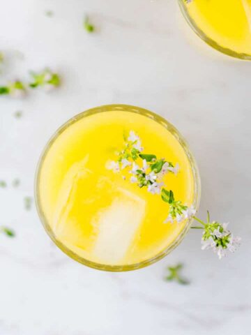 selbstgemachte mango limonade in einem glas mit eiswürfeln und thymian