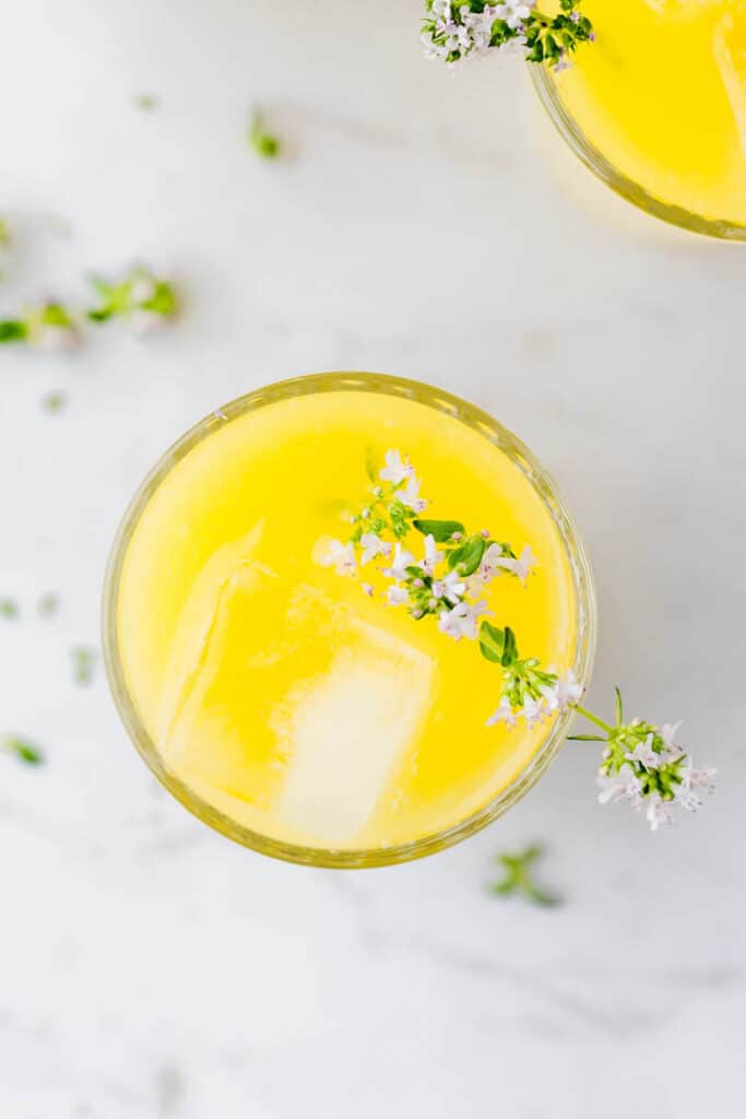 selbstgemachte mango limonade in einem glas mit eiswürfeln und thymian