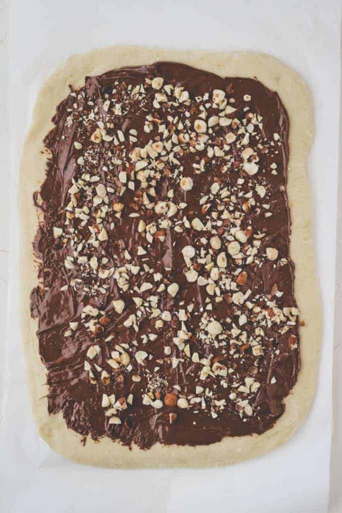 rolled out babka dough spread with nutella and topped with hazelnuts