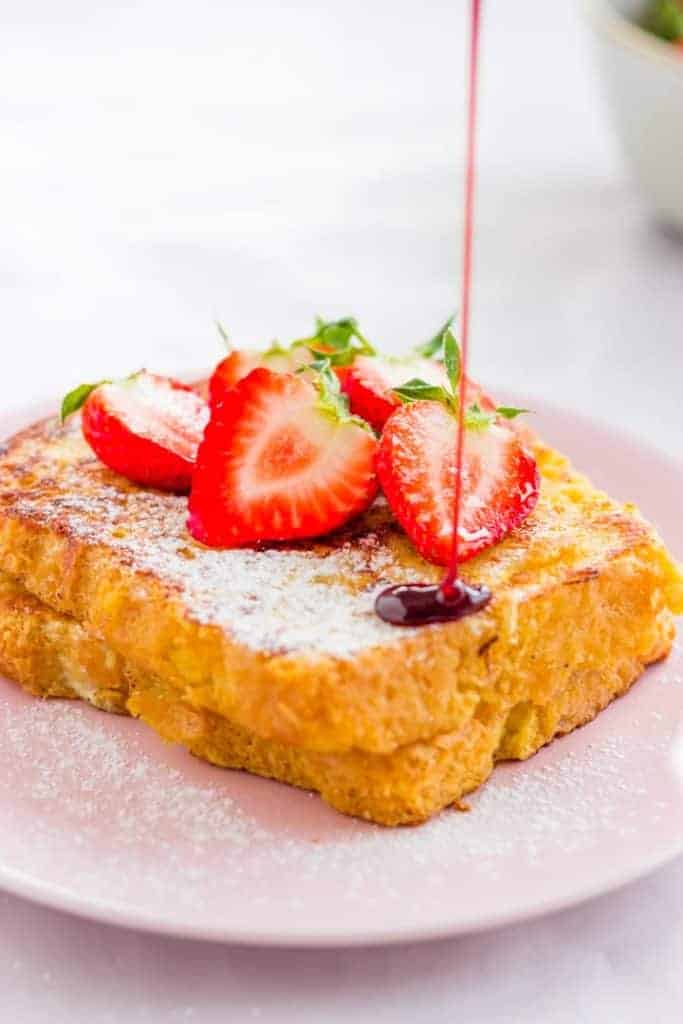 sweet french toast topped with strawberries and honey on a pink plate