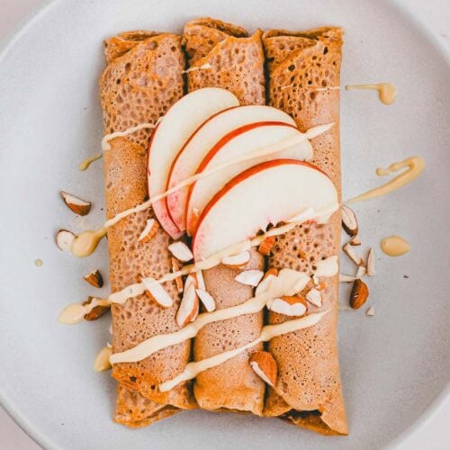 zusammengerollte buchweizen crepes auf einem teller mit nektarinen und mandelbutter dekoriert