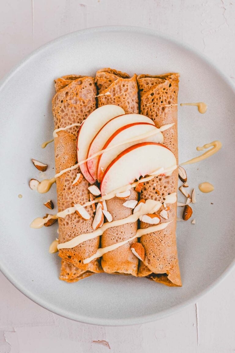 zusammengerollte buchweizen crepes auf einem teller mit nektarinen und mandelbutter dekoriert