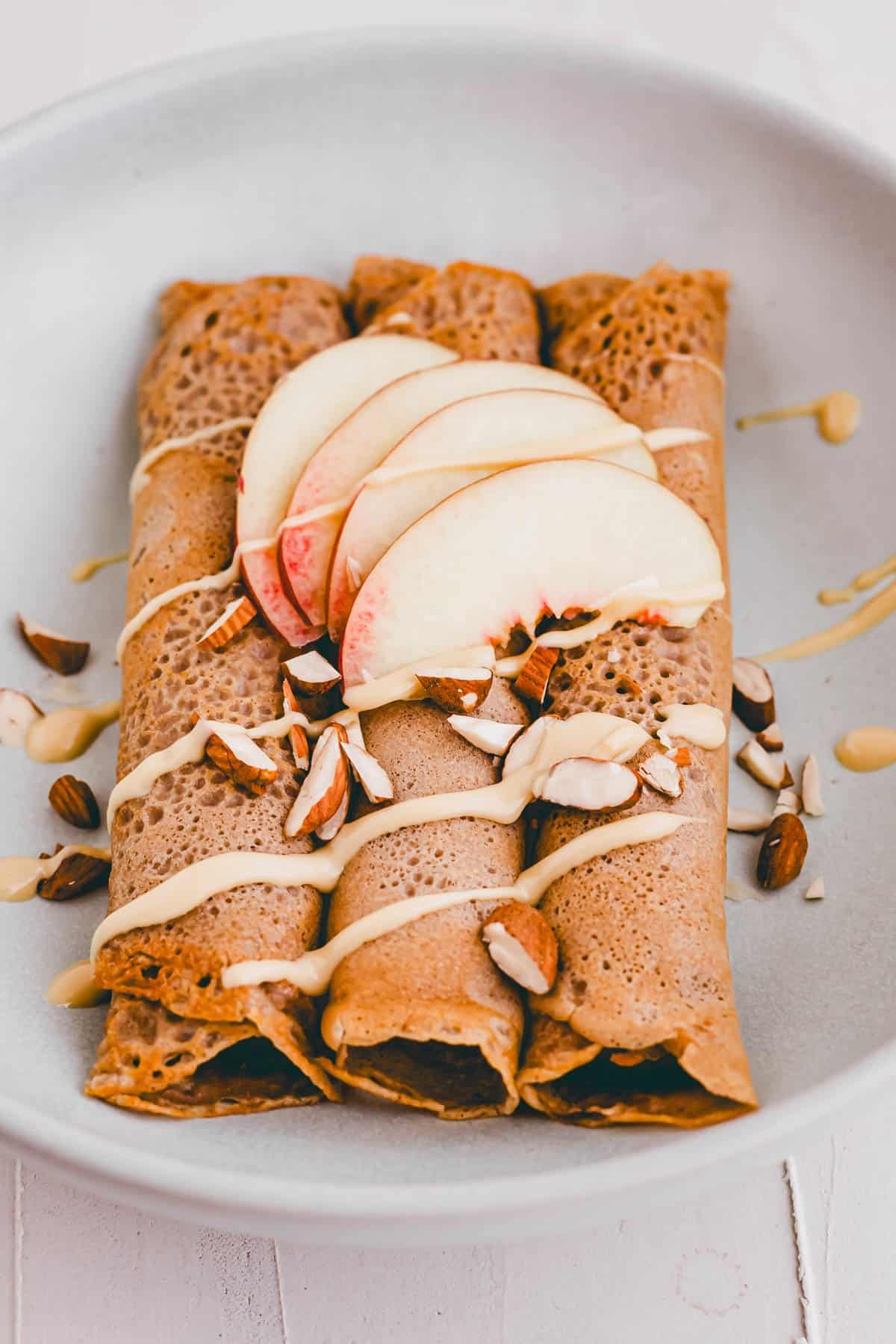 zusammengerollte buchweizen crepes auf einem teller mit nektarinen und mandelbutter dekoriert