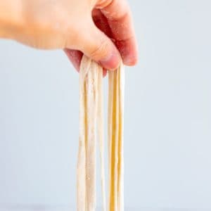 a hand holding raw homemade udon noodles