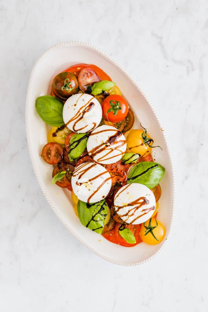 tomato burrata salad an a serving platter drizzled with balsamic glaze