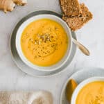 carrot ginger soup in bowl next to a piece of bread