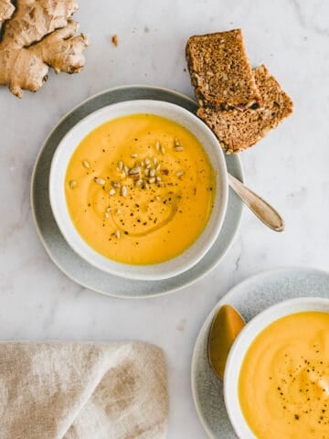 carrot ginger soup in bowl next to a piece of bread