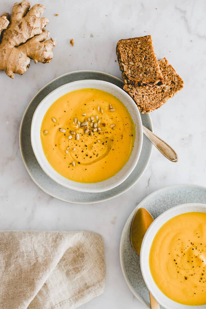 carrot ginger soup in bowl next to a piece of bread