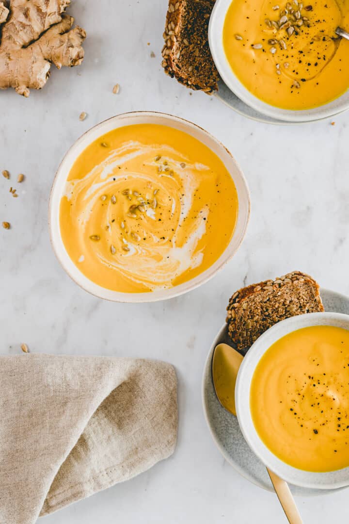 carrot and ginger soup in bowls with bread and ginger root by the side