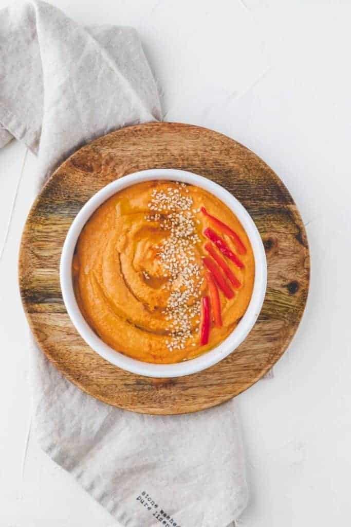 homemade roasted red pepper hummus topped with sesame seeds, olive oil, and roasted red peppers