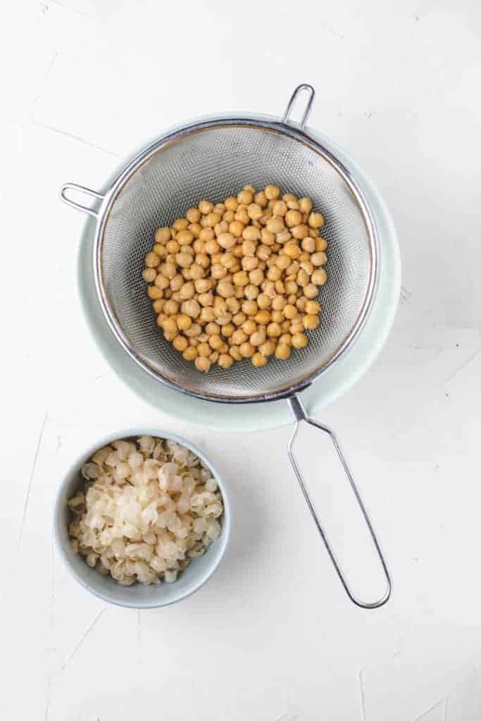 peeled canned chickpeas in a kitchen sieve next to the skin of the chickpeas