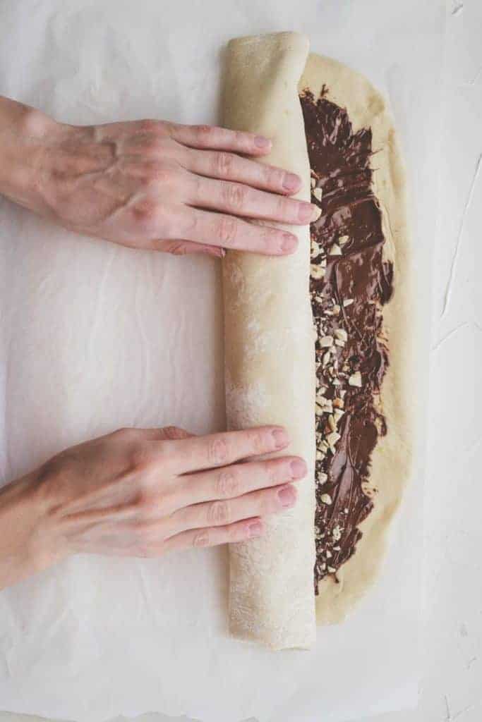 rolling up babka dough spread with nutella and topped with hazelnuts using hands