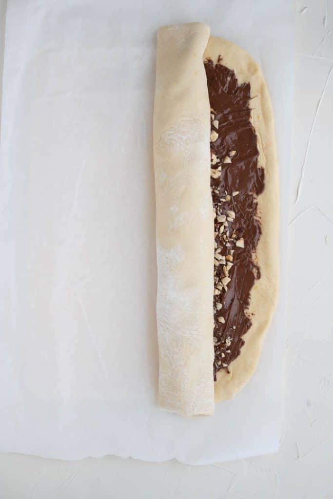 rolled up babka dough spread with nutella and topped with hazelnuts