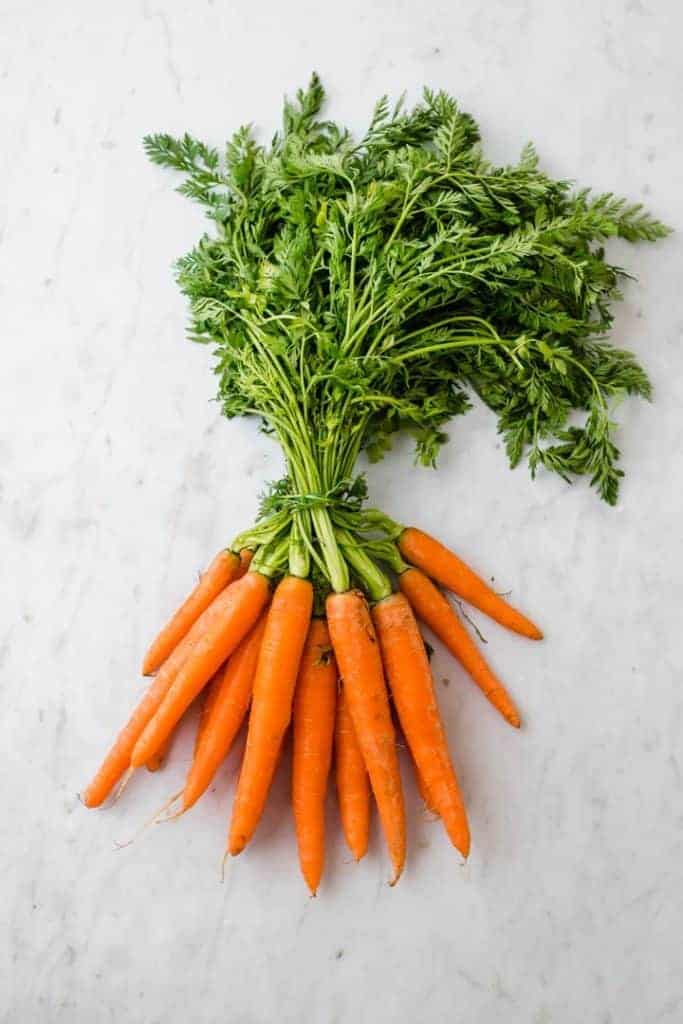 a bunch of carrots with green tops on a marble table