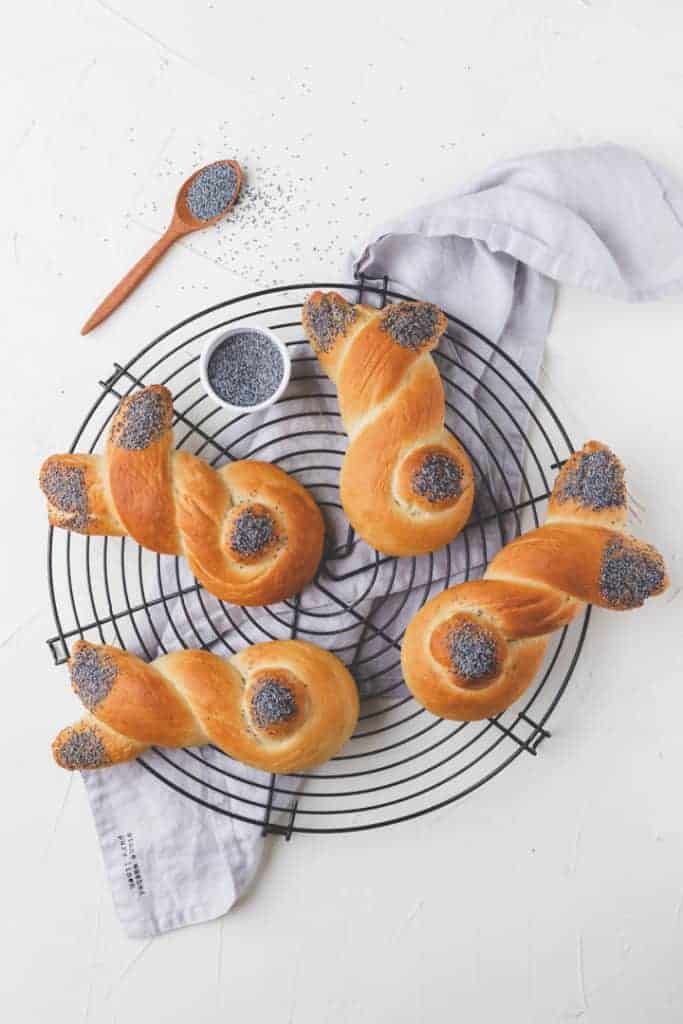 4 bunny bread rolls on a cooling wrack next to poppy seeds in a white bowl