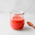 strawberry vinaigrette in a glass jar next to a wooden spoon