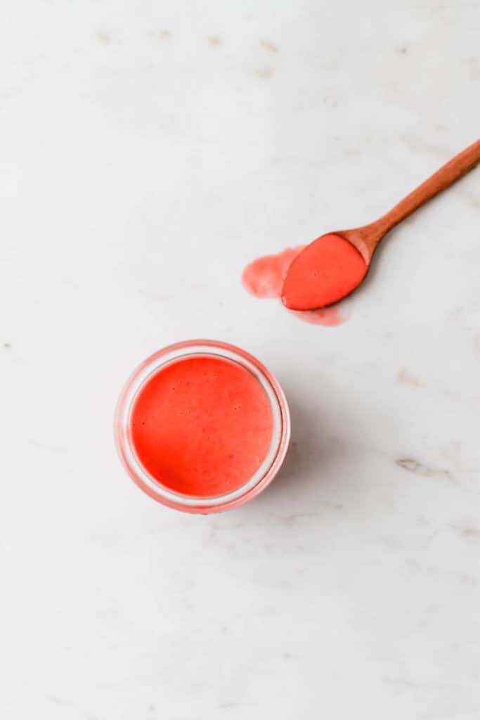 strawberry dressing in a glass jar next to a wooden spoon