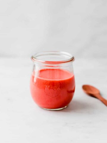 strawberry vinaigrette in a glass jar next to a wooden spoon