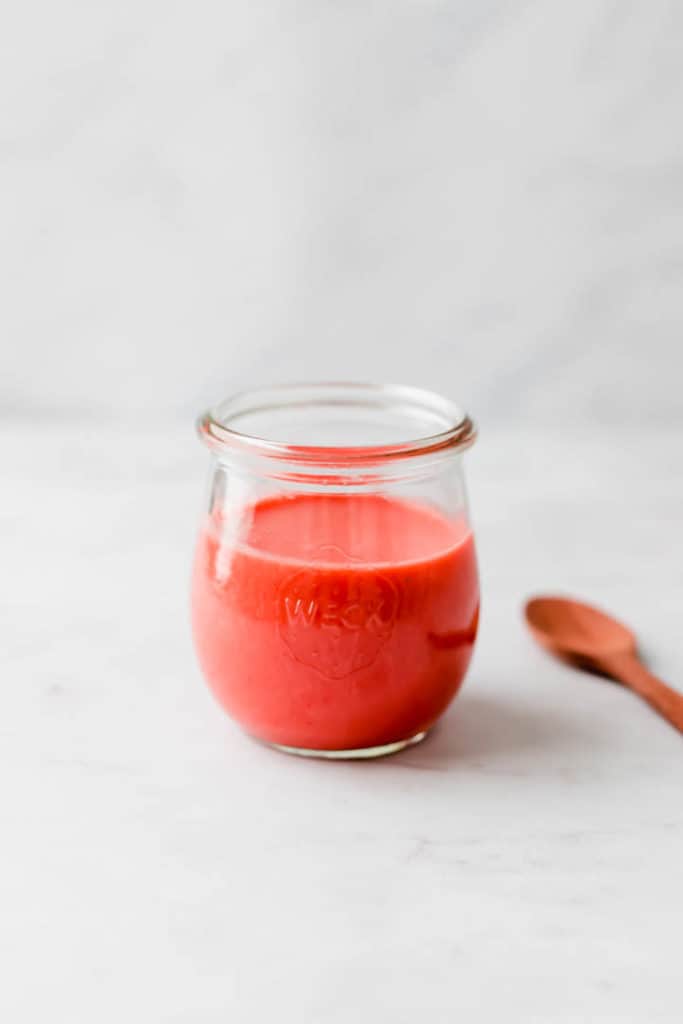 strawberry vinaigrette in a glass jar next to a wooden spoon