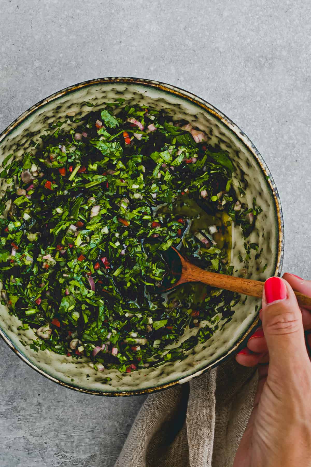 a hand holding a spoon with homemade chimichurri sauce