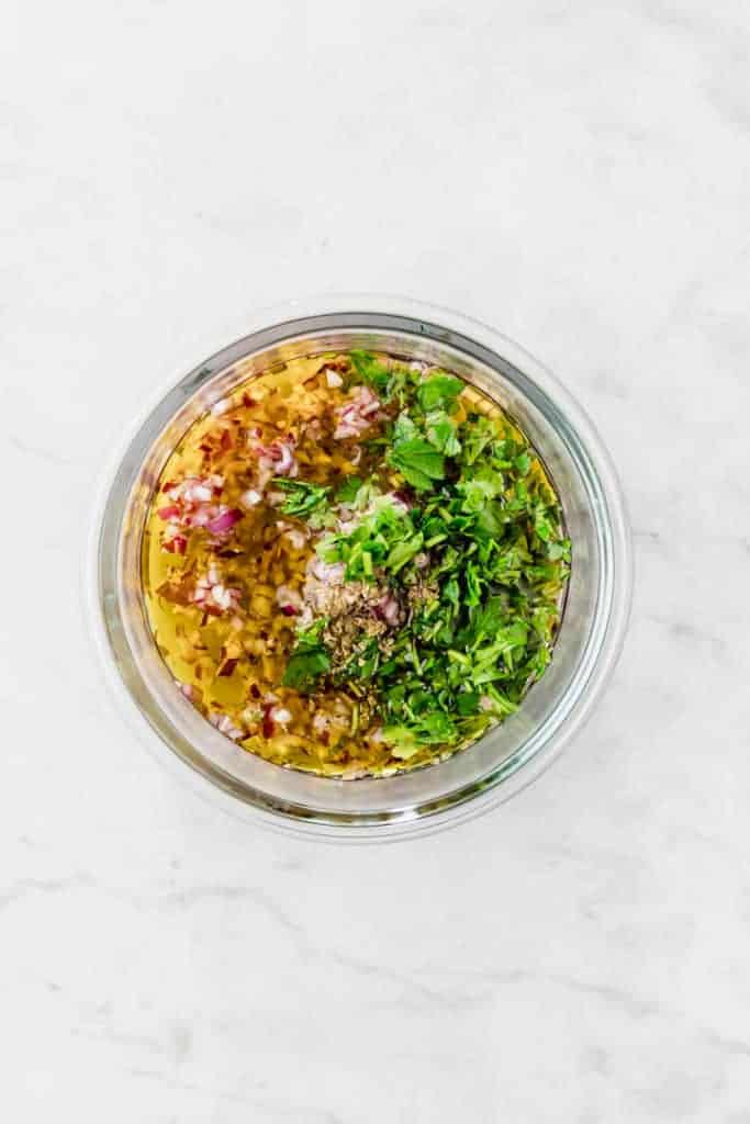 ingredients for chimichurri sauce in a glass bowl on a white table