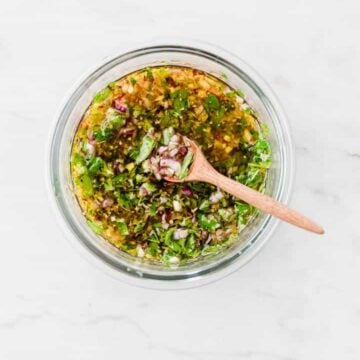 chimichurri sauce in a glass bowl with a brown wooden spoon