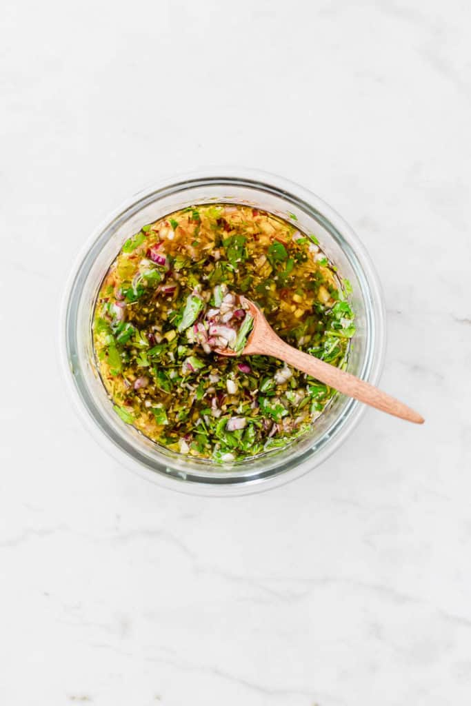 chimichurri sauce in a glass bowl with a brown wooden spoon
