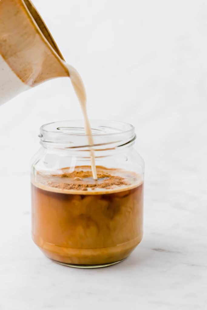 pouring oat milk into a jar full of coffee