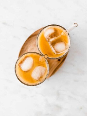 zwei gläser gefüllt mit eiskaffee und eiswürfel auf einem holzbrett