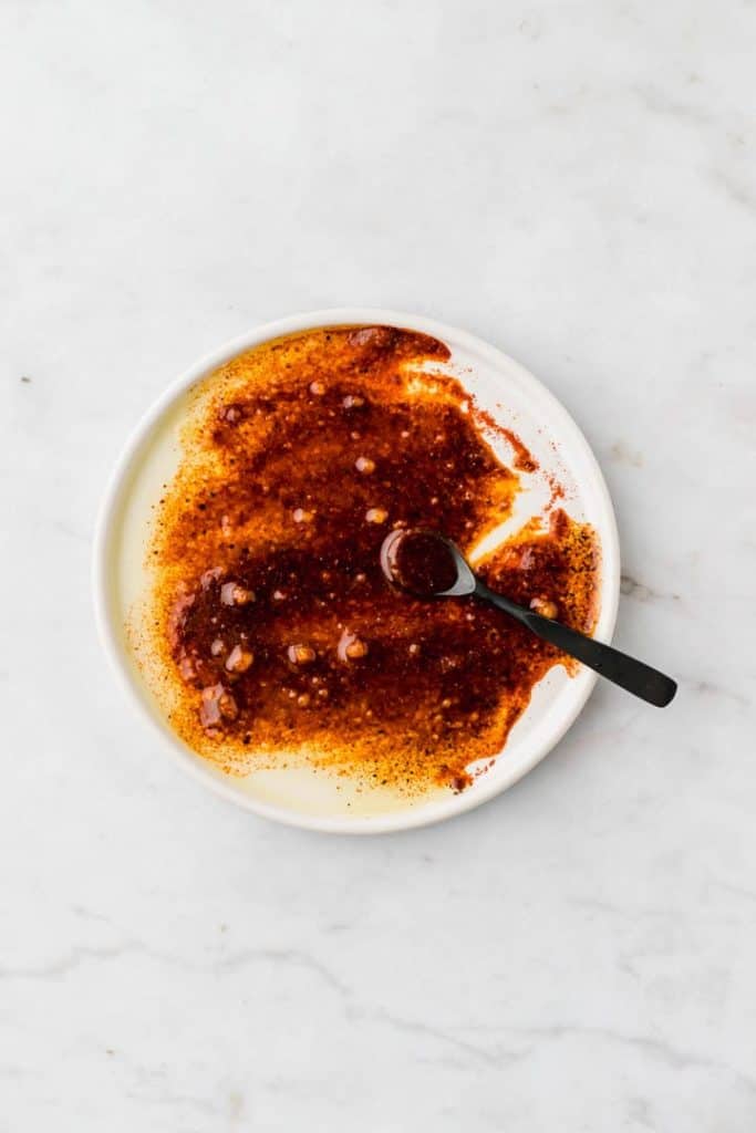 olive oil mixed with seasoning on a white plate with a black teaspoon