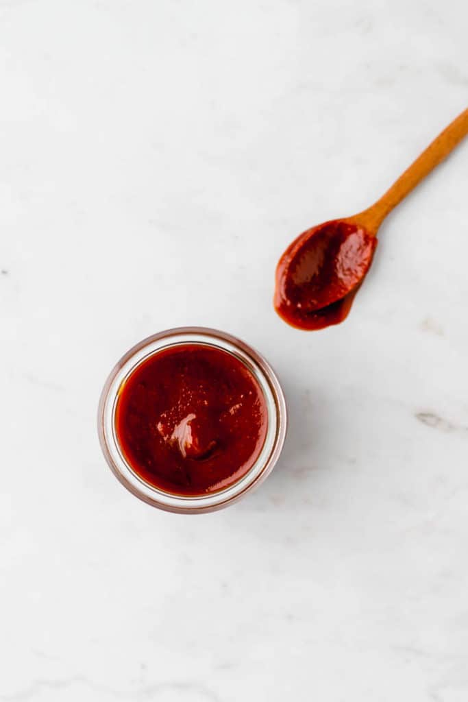 vegan bbq sauce in a jar next to a wooden spoon full of sauce
