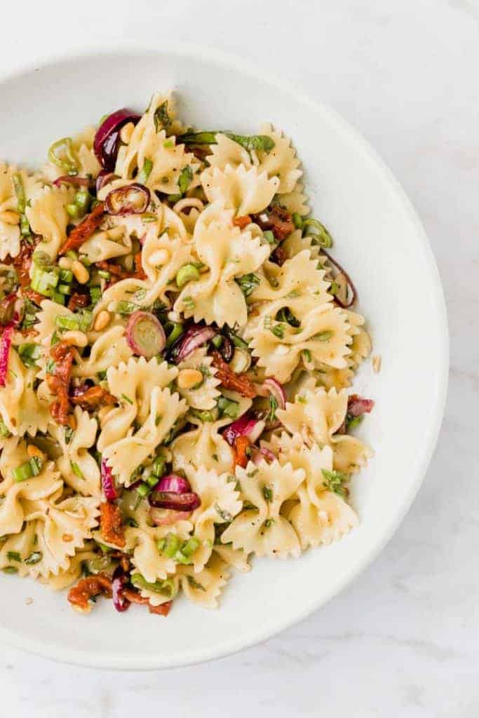 veganer nudelsalat mit sonnengetrockneten Tomaten, Pinienkernen, und Frühlingszwiebeln