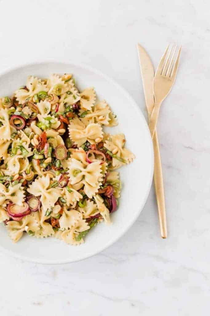 vegan bow tie pasta salad in a blue plate with golden cutlery next to it