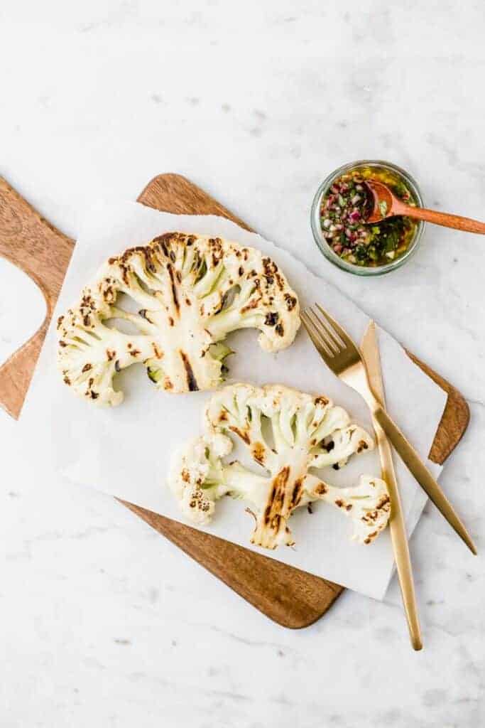 roasted cauliflower steak on a wooden board next to golden cutlery