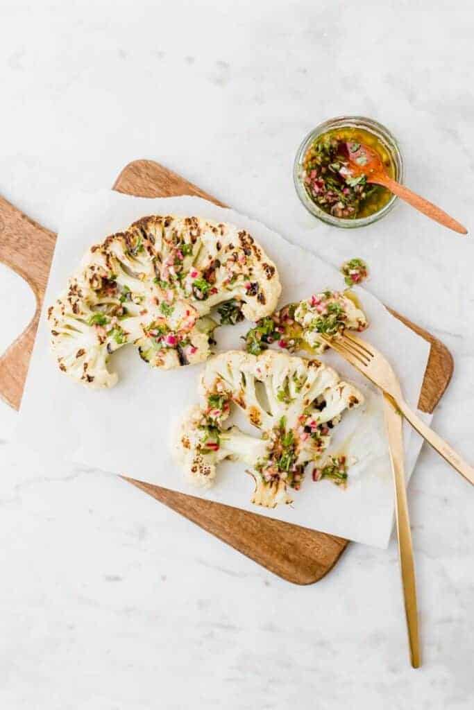 cauliflower steaks served with chimichurri on a wooden plate