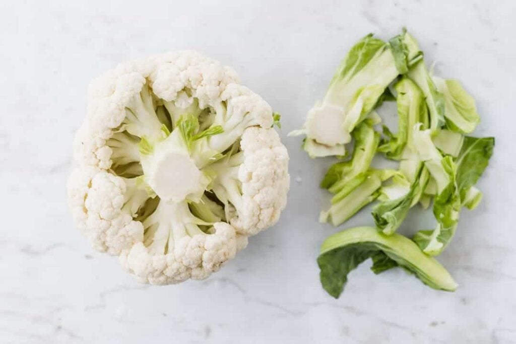 blumenkohl neben blumenkohl blätter auf einem weissen tisch