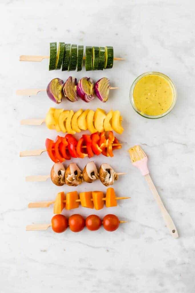 raw veggies on skewers next to marinade and a basting brush