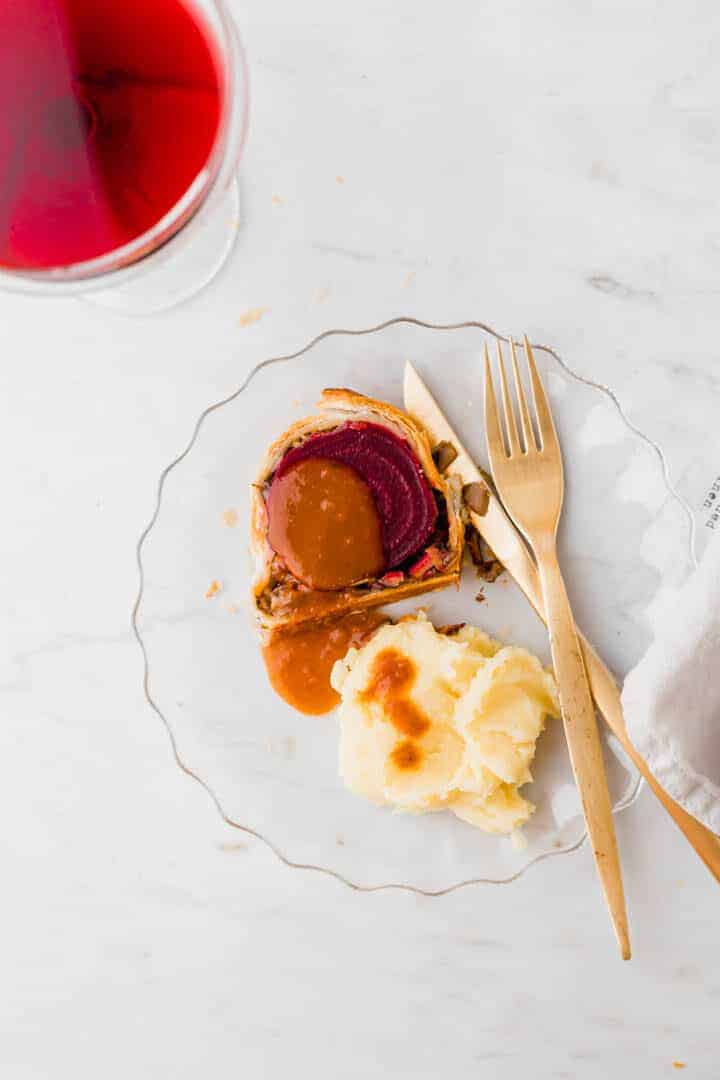 a slice beet wellington with gravy, mashed potato, and red wine