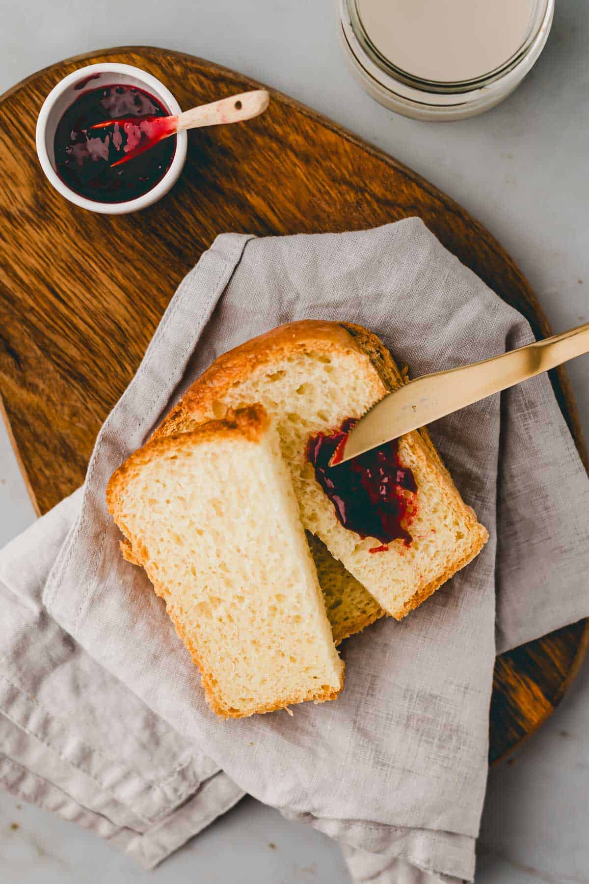 geschnittenes brioche brot auf einem holzbrett mit einem messer und marmelade