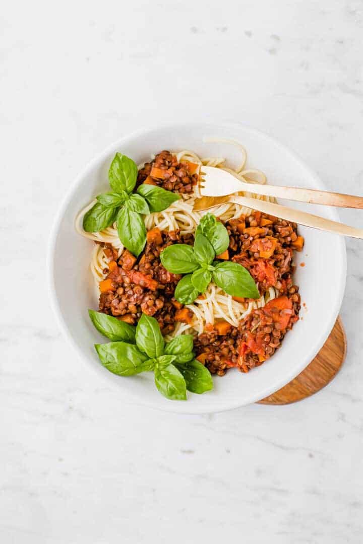 vegan bolognese served in a white bowl with spaghetti and golden cutlery