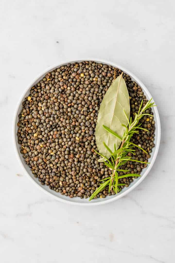 green puy lentils in a small blue bowl and fresh herbs