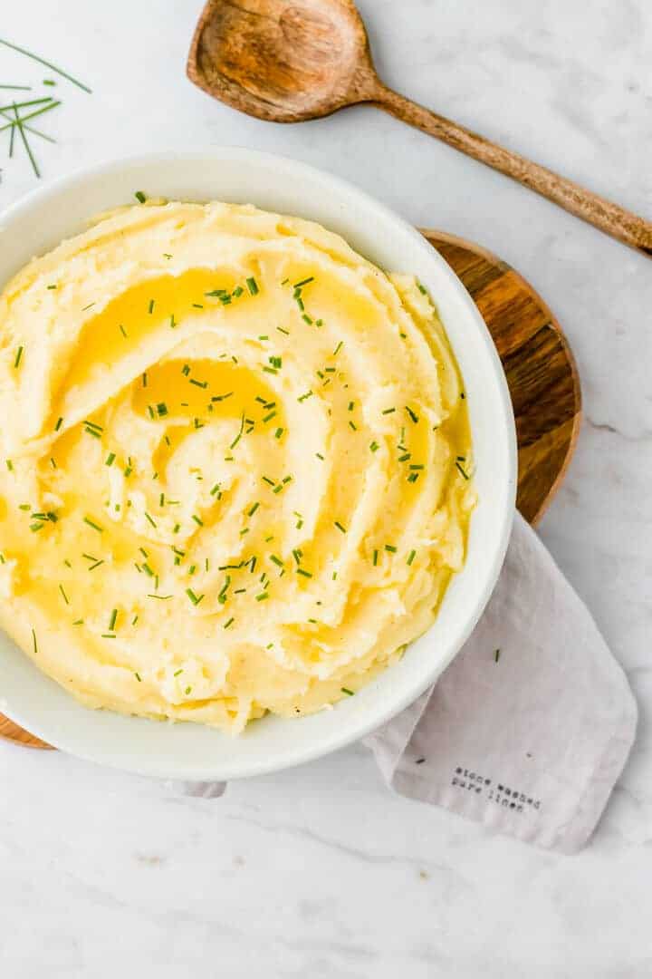 veganes kartoffelpüree servier in einem blauen teller mit schnittlauch und butter