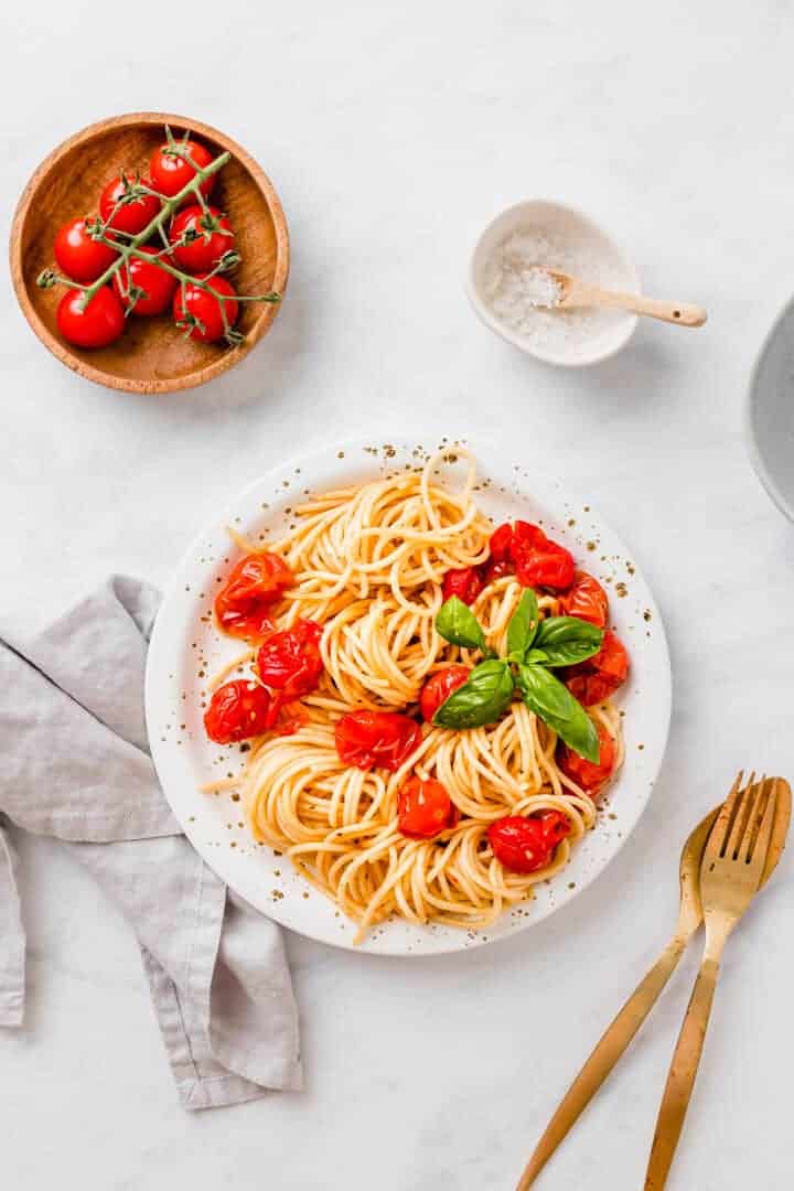 vegane spaghetti mit gerösteten cherry tomaten auf einem weissen teller serivert