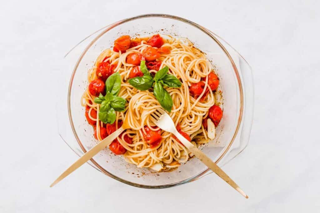 a baking dish full of cherry tomato pasta with golden cutlery