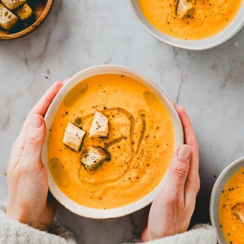 zwei hände halten eine schüssel mit karotten orangen suppe mit croutons