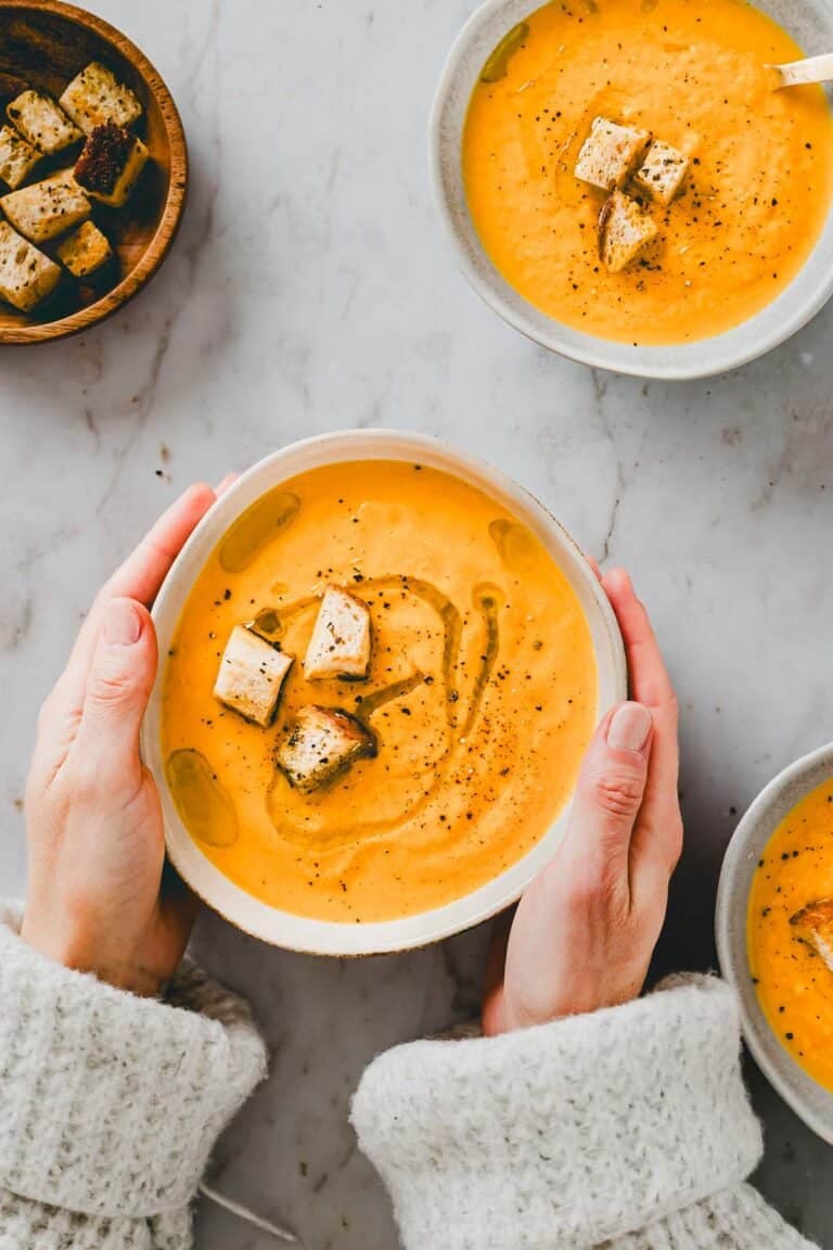 zwei hände halten eine schüssel mit karotten orangen suppe mit croutons