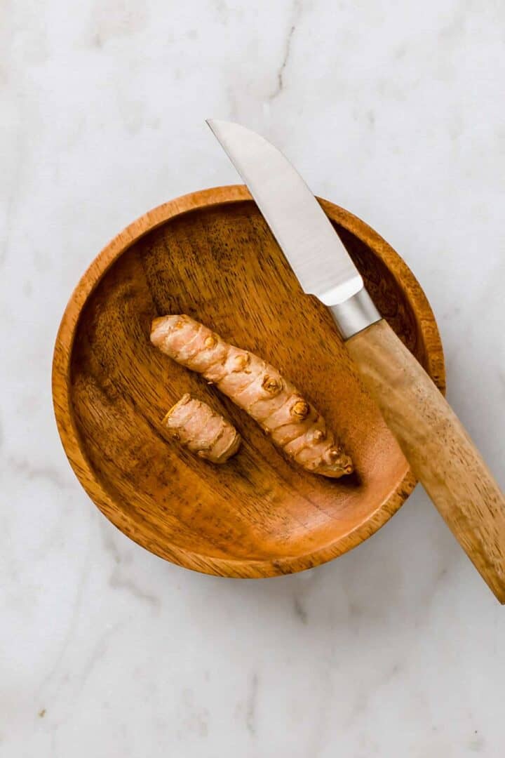 turmeric root in a small wooden bowl next to a knife