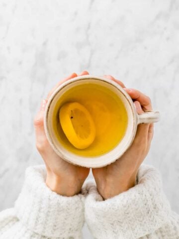 zwei hände halten eine tasse ingwer kurkuma tee